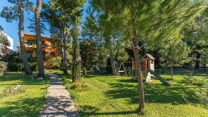 A pathway leading through a park with trees, a swing set, and a small wooden playhouse.