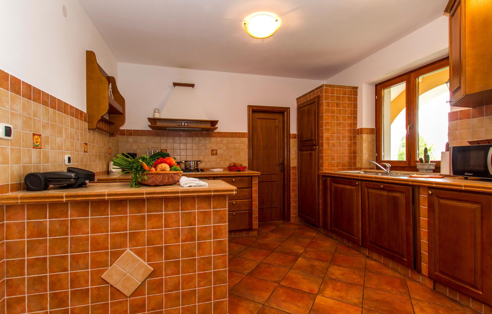 A kitchen with a tiled backsplash, wooden cabinets, a sink, and a countertop with a basket of fresh produce.