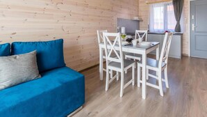 A cozy room with a blue sofa, a white dining table with chairs, and a kitchen area with a window and curtains. - Stunning home in Krynica Morska with WiFi (Krynica Morska)