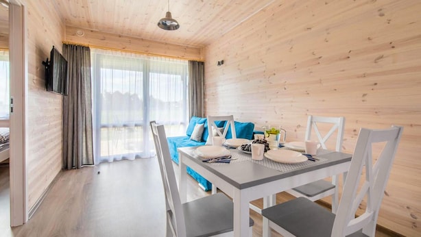 A cozy room with a dining table set for four, a sofa with blue cushions, and a large window with curtains. - Stunning home in Krynica Morska with WiFi (Krynica Morska)