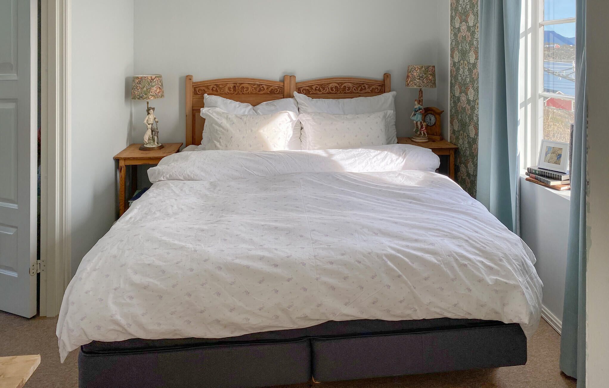 A neatly made bed with a floral-patterned duvet, wooden headboard, and two bedside tables with lamps and figurines.