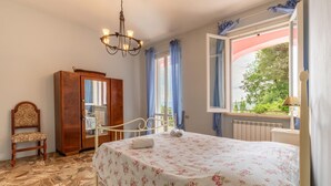 A bedroom with a bed, a wooden wardrobe, a chair, a chandelier, and a window with curtains. - Cozy home in Capolona (Capolona)