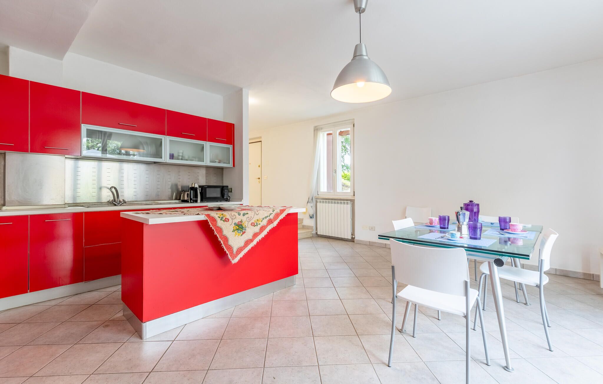 A modern kitchen with red cabinets and a glass dining table.