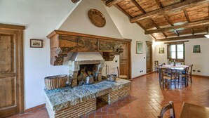 Una cocina rústica con chimenea de piedra, vigas de madera y un comedor con mesa y sillas.