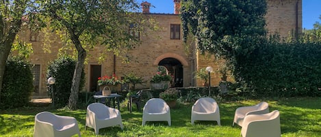 Un patio con paredes de piedra, un arco central y sillas de plástico blanco dispuestas en semicírculo.