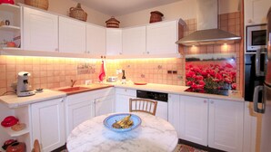 A kitchen with white cabinets, a marble island, a coffee maker, and a red vase with flowers. - Gorgeous home in Veyras (Veyras)