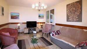 A living room with a television, two armchairs, a sofa, a glass coffee table, a chandelier, and artwork on the walls. - Gorgeous home in Veyras (Veyras)