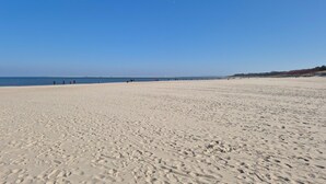 Una amplia playa arenosa con huellas y un cielo azul despejado.