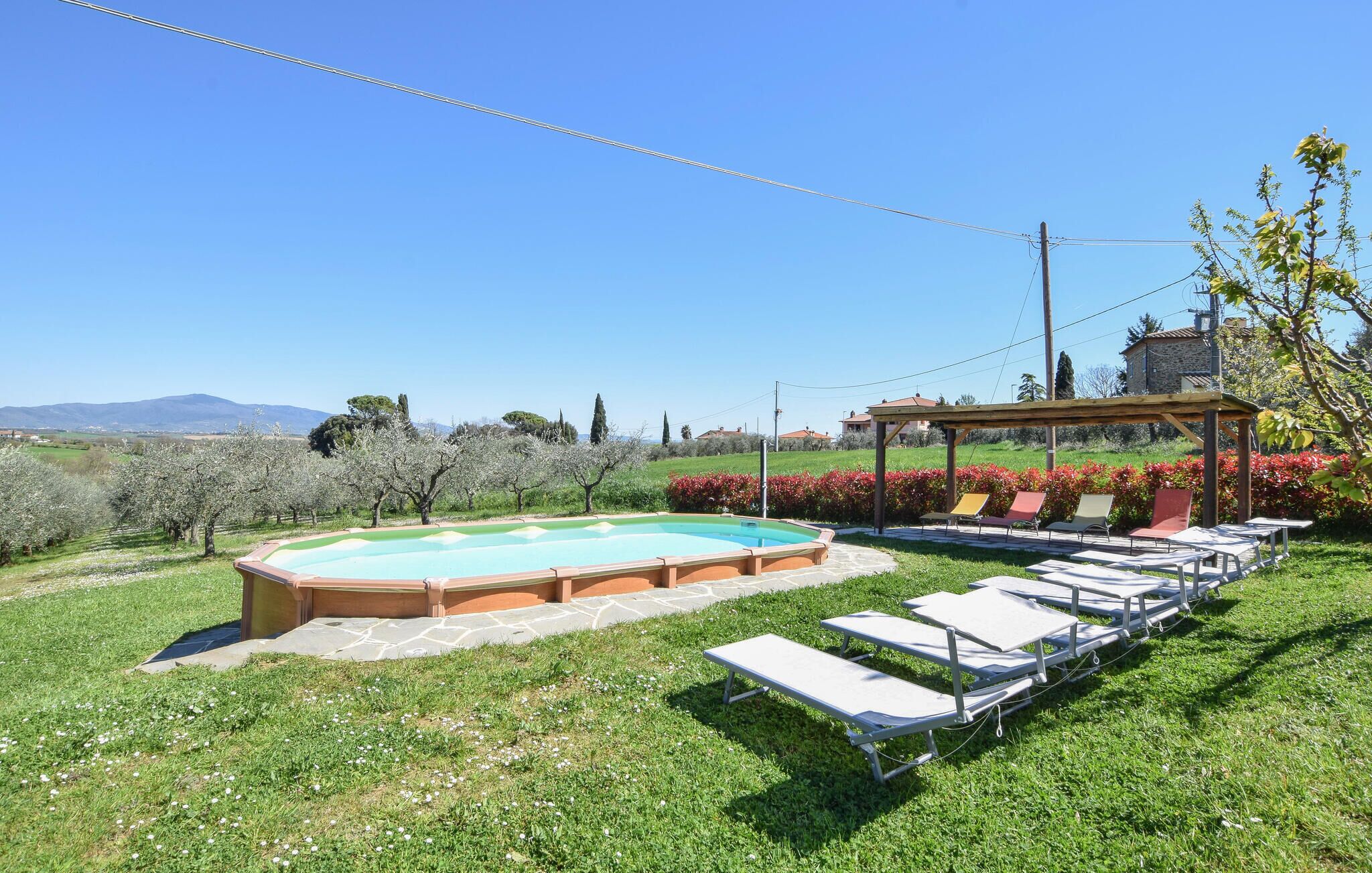 A swimming pool with lounge chairs and a pergola in a grassy area with a clear view of the countryside.