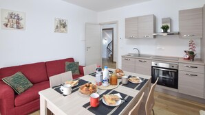 A modern kitchen with a dining area, featuring a red sofa, a table set with food, and a view of the adjacent living room. - Awesome home in Marciano della Chiana (Marciano della Chiana)