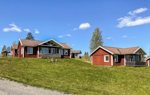 Een rij rode houten huizen met puntige daken, een grasveld en een helderblauwe lucht.
