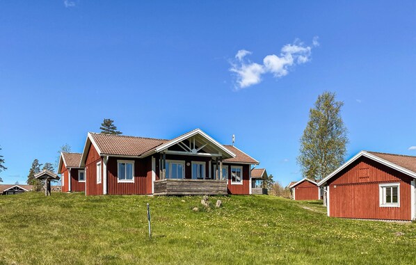 Een rode houten woning met een veranda, omgeven door een gazon en een helderblauwe lucht.