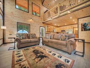 A spacious living area with two leather sofas, a wooden ceiling, and a view of the kitchen.