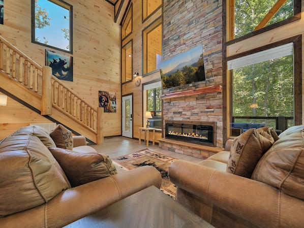 A spacious living area with leather sofas, a fireplace, wooden walls, and a staircase.