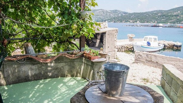 A rustic outdoor area with a concrete structure, a metal bucket, and a small boat docked by the water. - 2 bedroom lovely home in Zizanj (Zizanj)