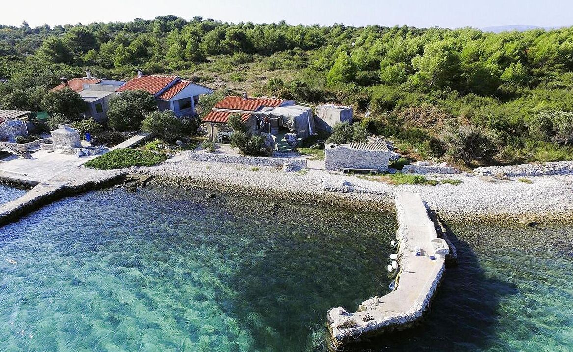 Une propriété située sur la côte, avec des eaux cristallines, un rivage rocheux et une maison avec un toit rouge.