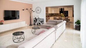 Un soggiorno moderno con una grande TV a schermo piatto, un divano, un tavolino da caffè e un'area pranzo con una cucina sullo sfondo.