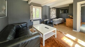 A modern living room with a leather sofa, a white coffee table, and a grey sofa. There is a TV mounted on the wall, a window with patterned curtains, and a wooden cabinet. - 2 bedroom nice home in Huaröd (Huaröd)