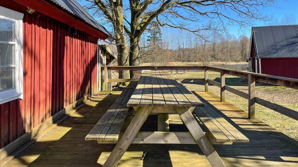 A wooden picnic table with benches on a deck, surrounded by red wooden buildings. - 2 bedroom nice home in Huaröd (Huaröd)