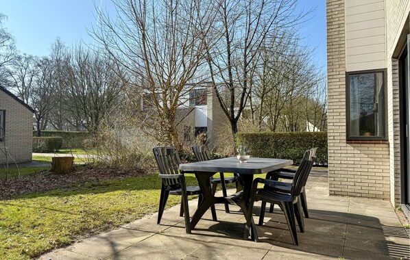 Une terrasse extérieure avec une table et des chaises, entourée d’une pelouse et d’arbres.
