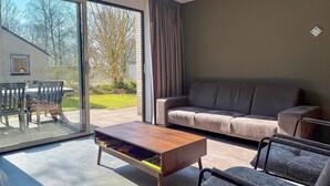 A modern living room with a sofa, chairs, a coffee table, and a sliding glass door leading to a patio. - 3 bedroom stunning home in Hoeven (Hoeven)