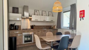 A modern kitchen with a dining area, stainless steel appliances, and a hanging light fixture. - 3 bedroom stunning home in Hoeven (Hoeven)
