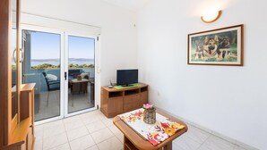 A room with a sliding glass door leading to a balcony, a television on a wooden stand, a framed picture on the wall, and a small table with a vase. - Gorgeous apartment in Baska Voda with WiFi (Baska Voda)