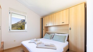 A neatly made bed with pillows and towels, wooden wardrobe, and a window with a mountain view. - Gorgeous apartment in Baska Voda with WiFi (Baska Voda)