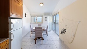 A kitchen with wooden cabinets, a dining table with chairs, a window with a view, and a sliding glass door leading to a balcony. - Gorgeous apartment in Baska Voda with WiFi (Baska Voda)
