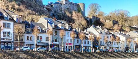 A riverside town with historic stone buildings, a castle on a hill, and a pedestrian walkway.