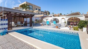 Un espace piscine doté d’une terrasse carrelée, de chaises longues et d’une structure en forme de pergola.