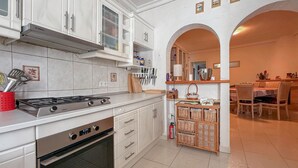 Une cuisine moderne avec des meubles blancs, une cuisinière à gaz Bosch et un four. On y trouve des meubles en bois avec des portes en verre et un petit coin repas avec une table et des chaises.