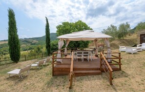 Un espacio de estar rústico al aire libre con una mesa y sillas de madera, rodeado por una cerca de madera y un toldo.