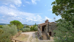 Un edificio rústico de piedra con tejado de baldosas, una reja de madera y un camino empedrado que lleva a él.