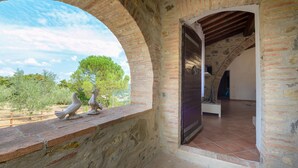 Una habitación rústica con paredes de ladrillo visto, suelo de baldosas y vistas al verdor exterior.