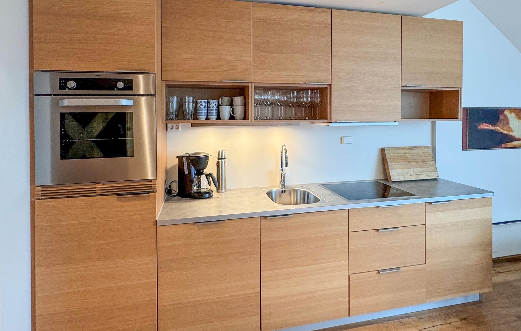 A modern kitchen with wooden cabinets, a built-in oven, a coffee maker, and a sink.