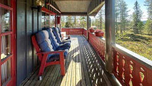 A wooden deck with a red railing, a bench with blue cushions, and a view of a forest. - Beautiful home in Jordet with sauna (Jordet)