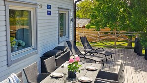 A deck with a table set for dining, outdoor chairs, and a view of a garden.