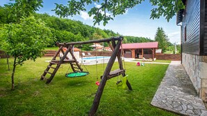 En gungställning i trä på en gräsplätt, med en pool och en byggnad i bakgrunden.