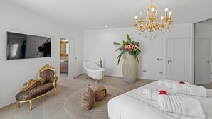 A modern bedroom with a large bed, a vanity with a bathtub, a leopard-print chair, a chandelier, and a large vase with flowers. - Lovely home in Galizana with sauna (Galizana)