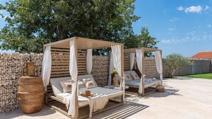 Two outdoor wooden canopy beds with white curtains, a large terracotta pot, and a stone wall backdrop. - Lovely home in Galizana with sauna (Galizana)