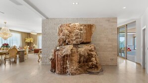 A modern interior with a large rock sculpture, a dining area with a chandelier, and a view through a glass door. - Lovely home in Galizana with sauna (Galizana)
