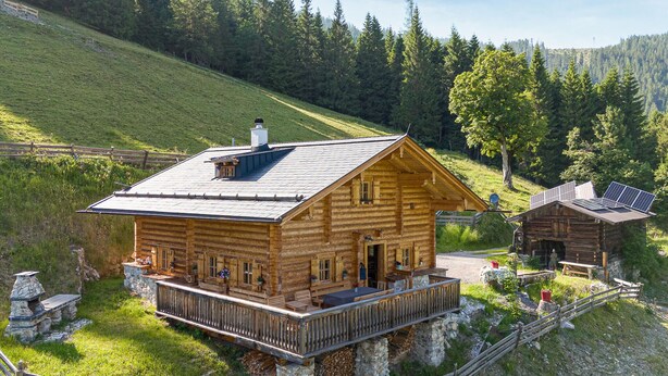 Una cabaña de madera con balcón, paneles solares y base de piedra.