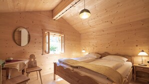 Un dormitorio de cabaña de madera con cama, escritorio, silla, lámpara y ventana.