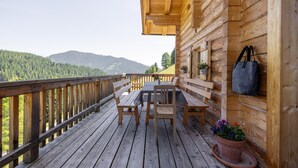 Una terraza de madera con una mesa y sillas, con vista a una cadena montañosa boscosa.