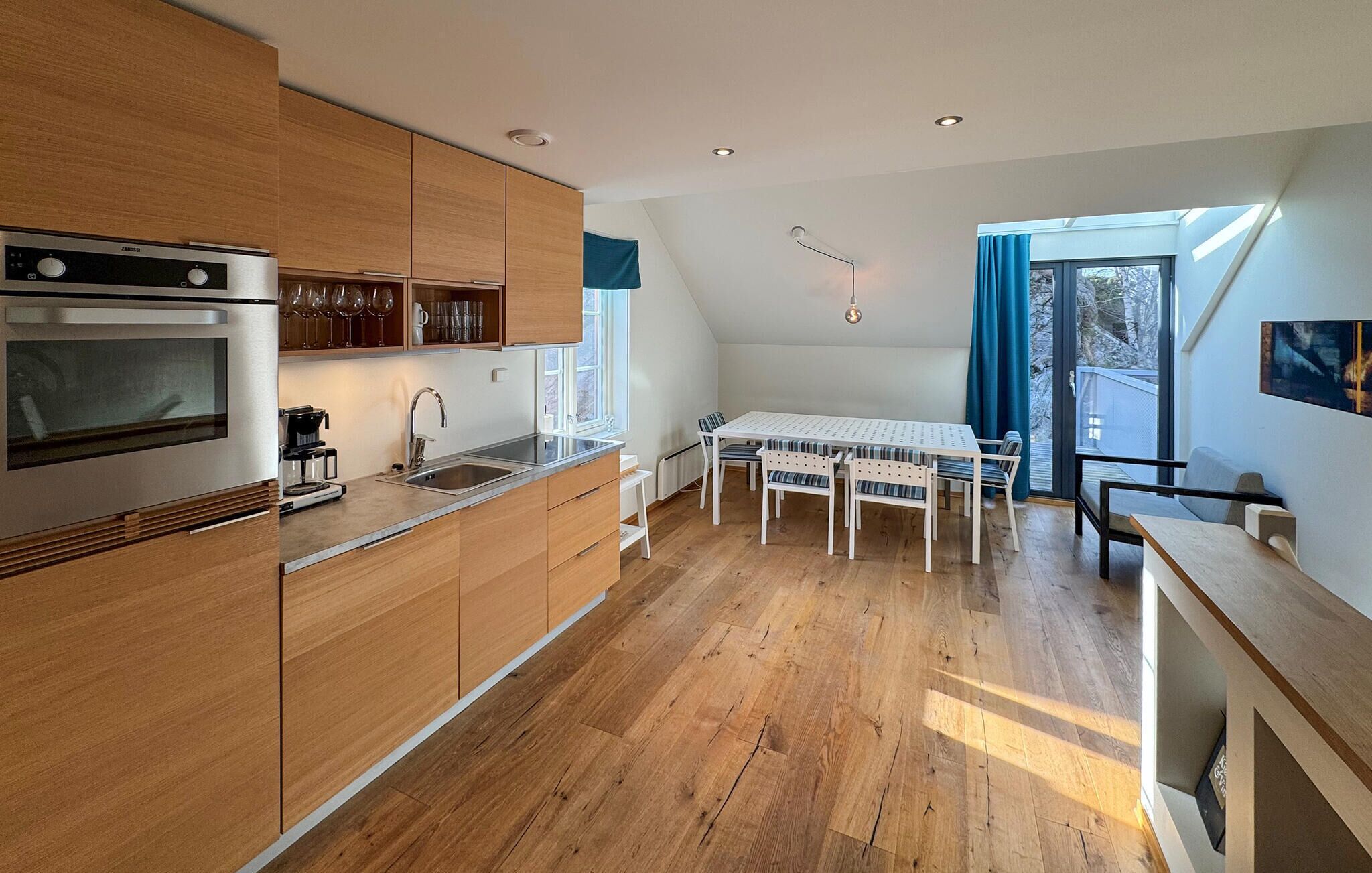 A modern kitchen with wooden cabinets, a built-in oven, and a dining area with a table and chairs.