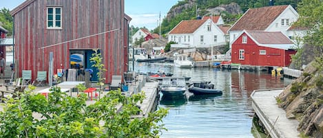 A waterfront scene with a wooden building, boats, and houses.