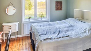 Une chambre à coucher comprenant un lit, une commode, un miroir, une fenêtre donnant sur des arbres et un radiateur.
