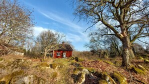 Une maison en bois rouge, entourée d’arbres et de rochers.
