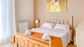 A bedroom with a bed, a radiator, a painting, and a window with curtains.